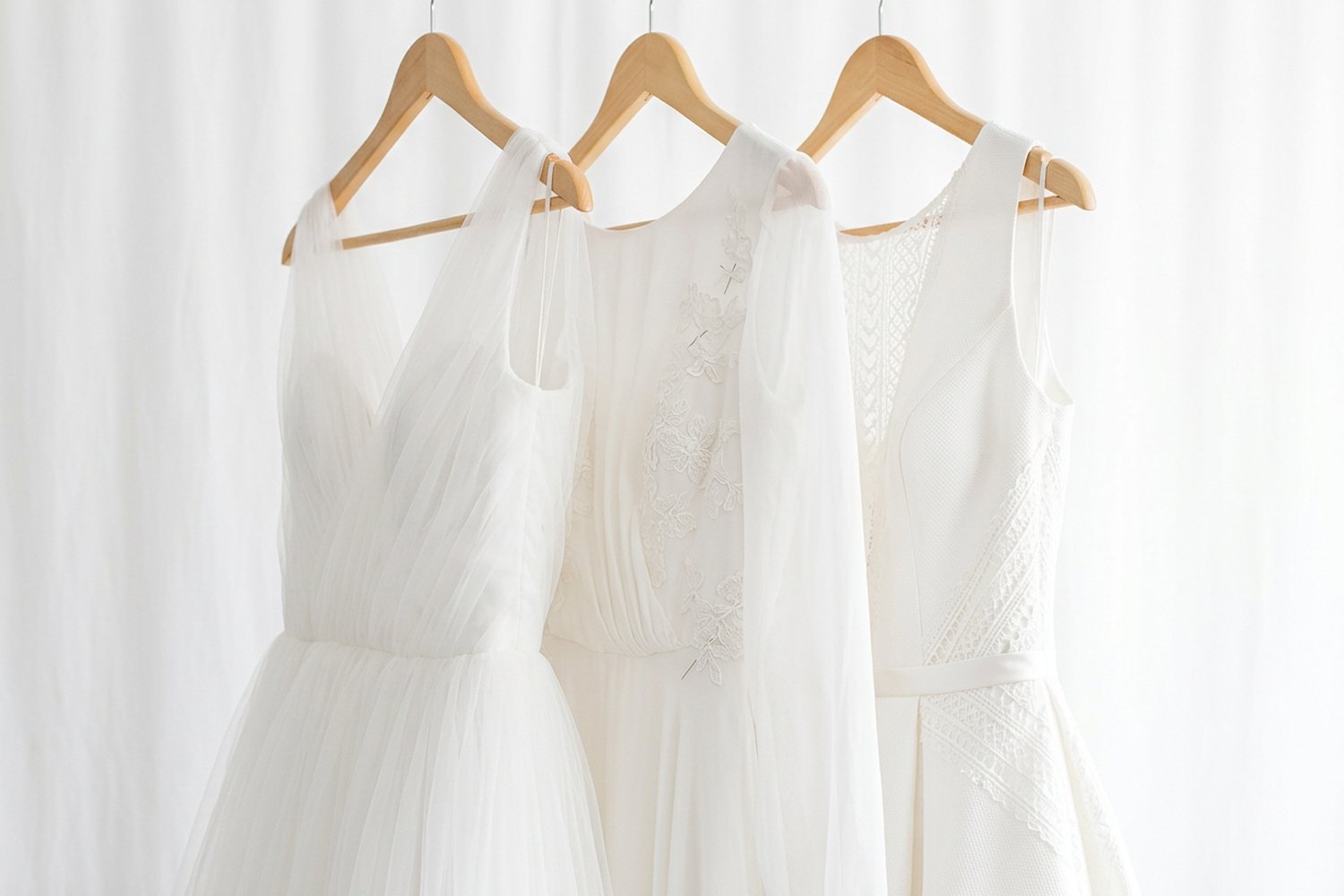 Trois robes suspendues à des cintres de bois, distinguées par leurs textures : tulle plissé, crêpe et dentelle, maille ajourée.
