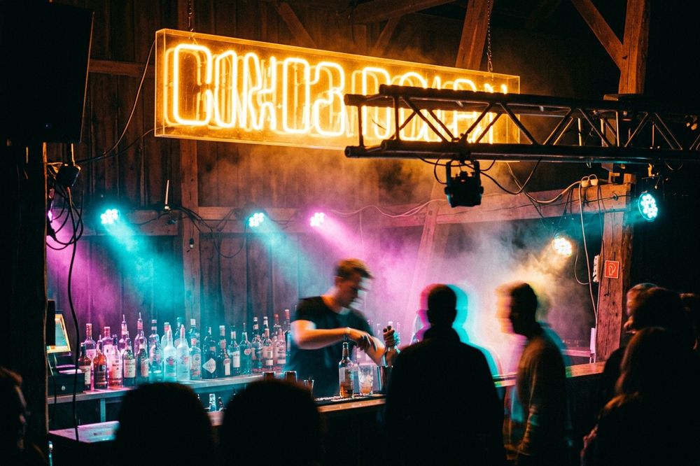 Bar de nuit sous une enseigne au néon ambre, silhouettes devant.