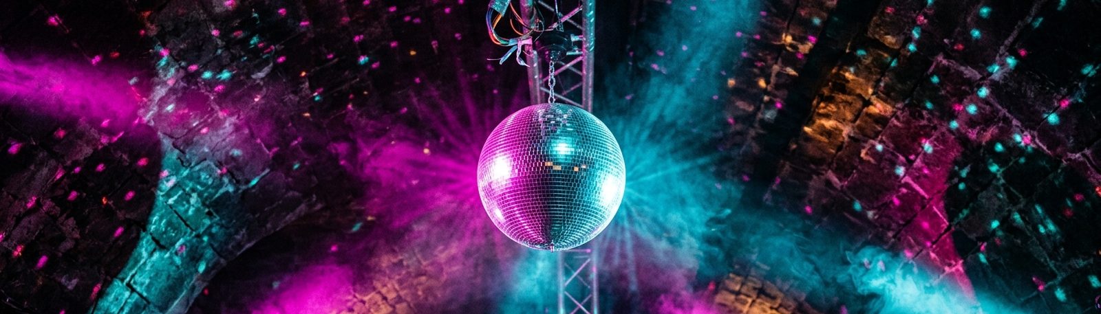 Boule à facettes sous une voûte de pierre, points de lumière magenta et cyan dans la fumée.