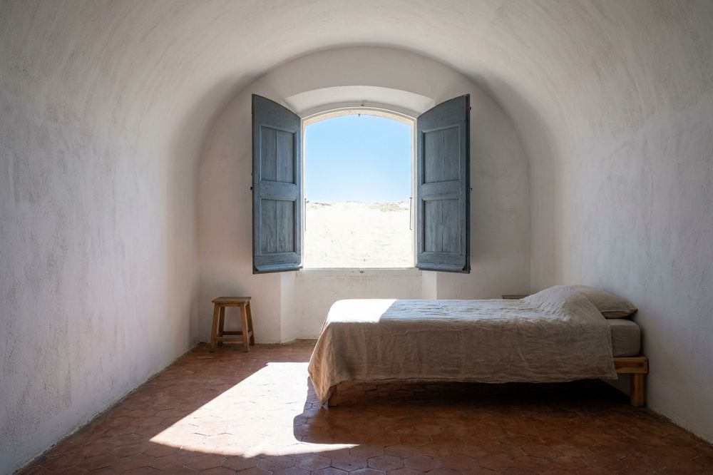 Chambre voûtée à la chaux, volets grands ouverts, rectangle de soleil au sol.